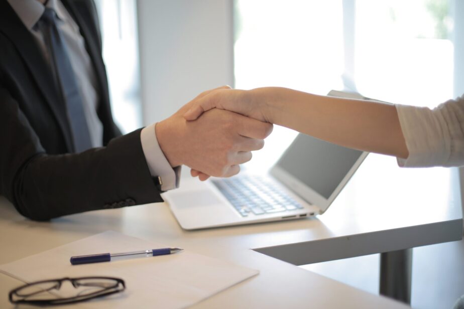 A picture of a white man shaking a white woman's hand at a job interview. Learn what questions to ask at the end of an interview.