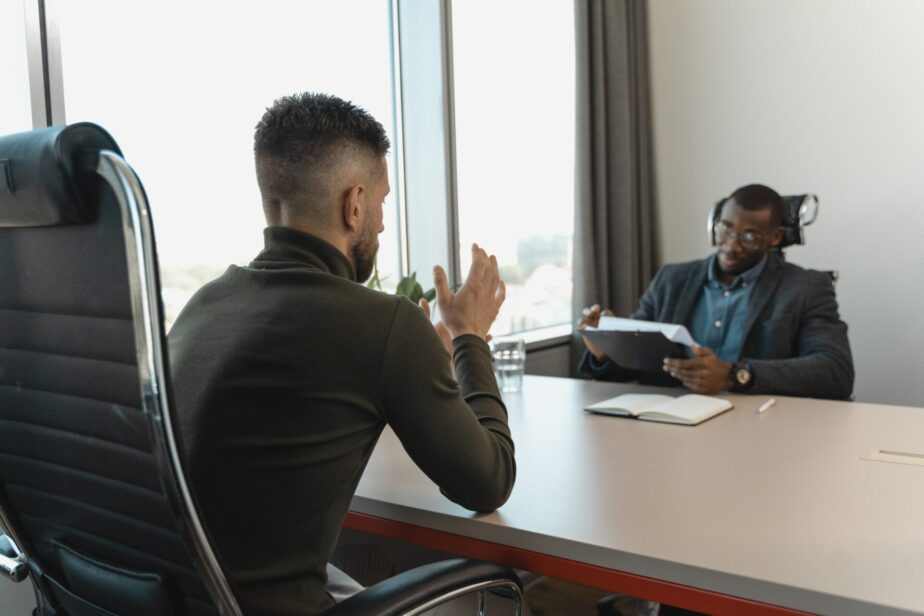 A picture of a job interview with a black man interviewing a white man. Learn what questions to ask at the end of an interview.