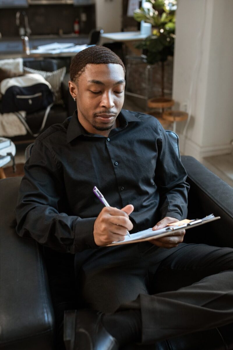 A picture of a black man (the interviewer) in smart black button shirt writing on a clip board containing an interview scorecard. Learn what questions to ask at the end of an interview.