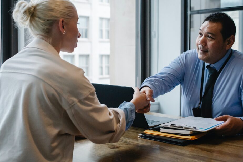 A picture of an Asian man (the interviewer) shaking a white woman's hand at a job interview. Learn what questions to ask at the end of an interview.