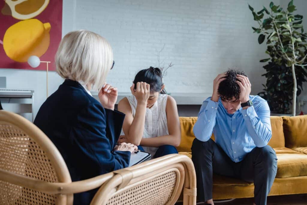 An image of a team in conflict and trying to bring a resolution to their employment issues. A male and female staff member have their head in their hands. Another female staff member is mediating the conflict. An AI Coach can help to handle employment issues.