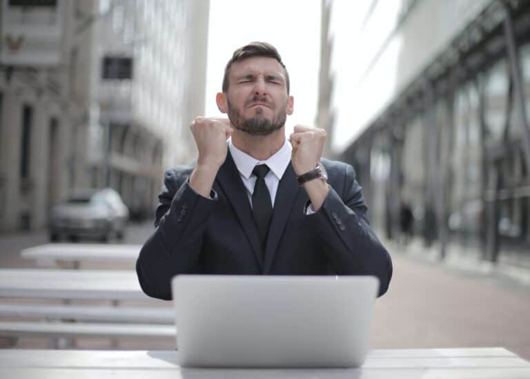 A man celebrates success after securing a job after using an AI Interview Coach. The man is wearing a suit and sitting in front of a computer.