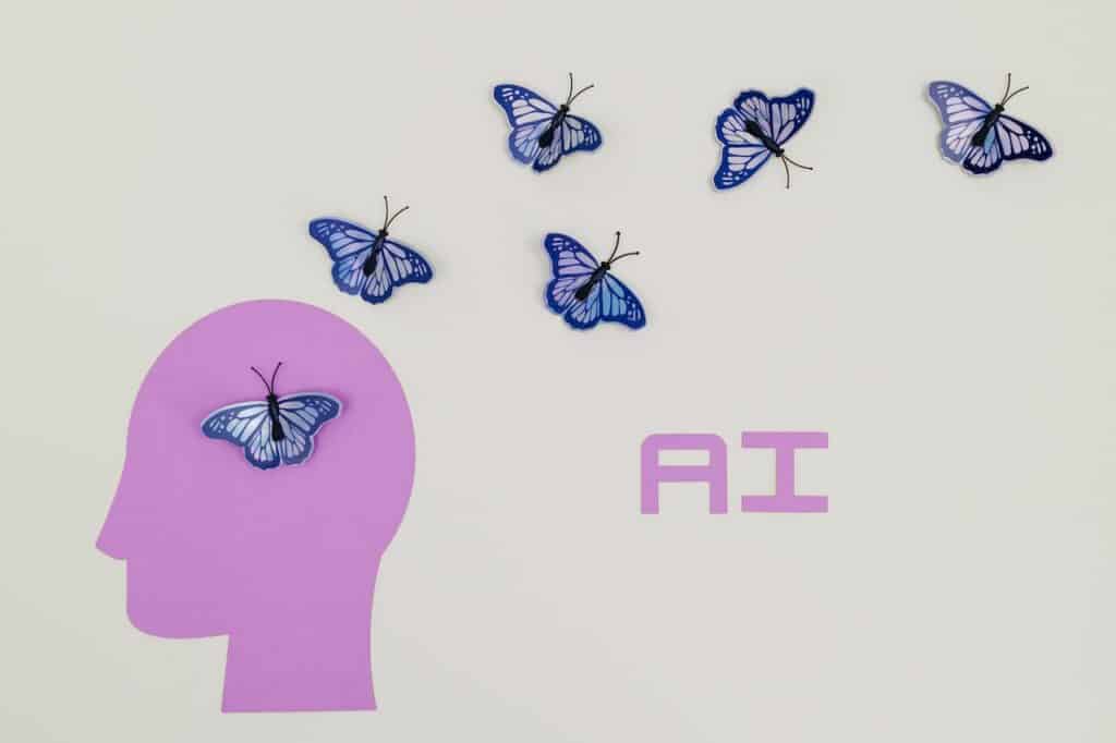 An image of a purple human head, with butterflies flying out of the head and the word "AI" in purple.  This image represents upskilling yourself in AI, which is important when considering how to get into AI.