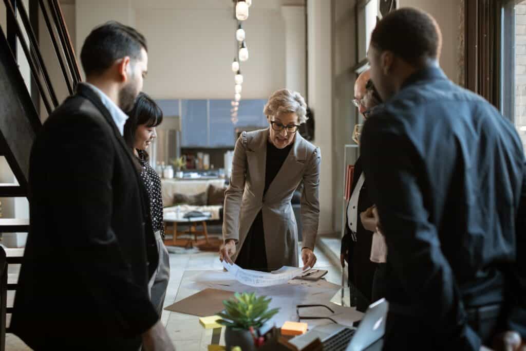 A group of team members standing in circle discussing something which is on the table.